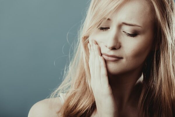 close up of woman with blonde hair touching face because of toothache
